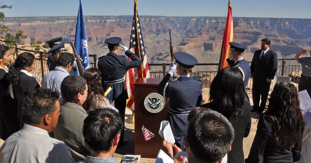 Ceremonia de naturalización al aire libre, con guardia de honor y candidatos sentados frente a un podio