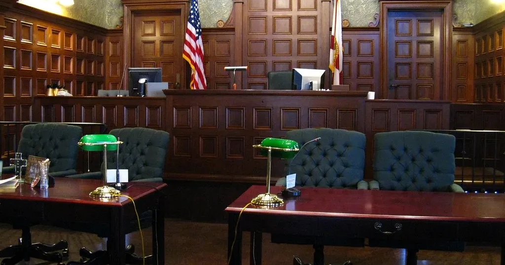 Sala de corte vacía con paneles de madera, banderas de Estados Unidos y de Florida, y las mesas de los abogados