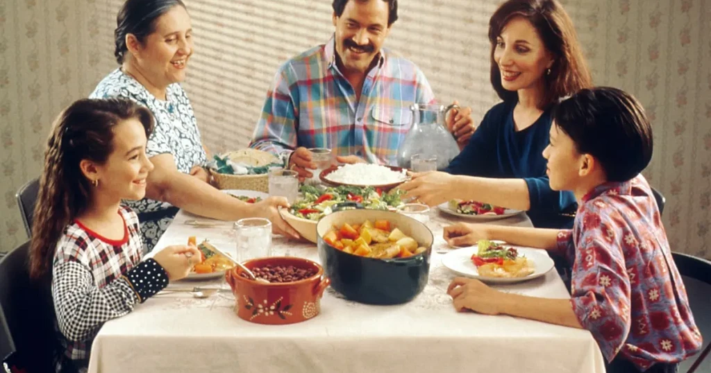 Family of five sharing a meal around a dining table, passing dishes to one another