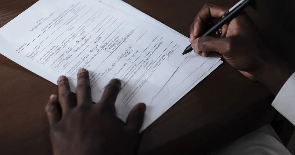 Close-up of a person signing a printed application form at a wooden desk