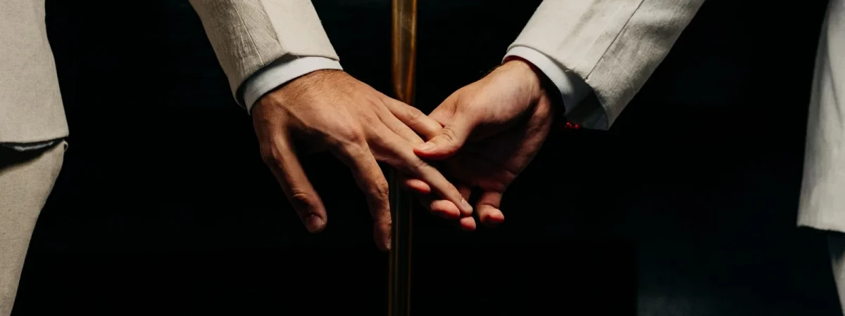 Hands of a same-sex couple in white suits at their wedding ceremony — same-sex marriage green cards and SOGI asylum, Immigration Law Center Orlando