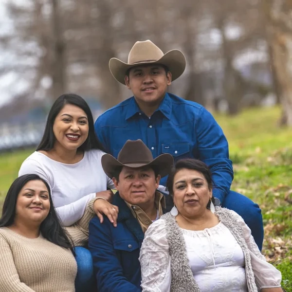 Familia de cinco personas posando al aire libre en un campo, dos de ellos con sombreros vaqueros