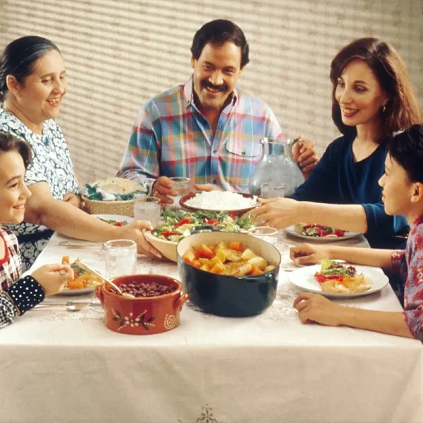 Family of five sharing a meal around a dining table, passing dishes to one another