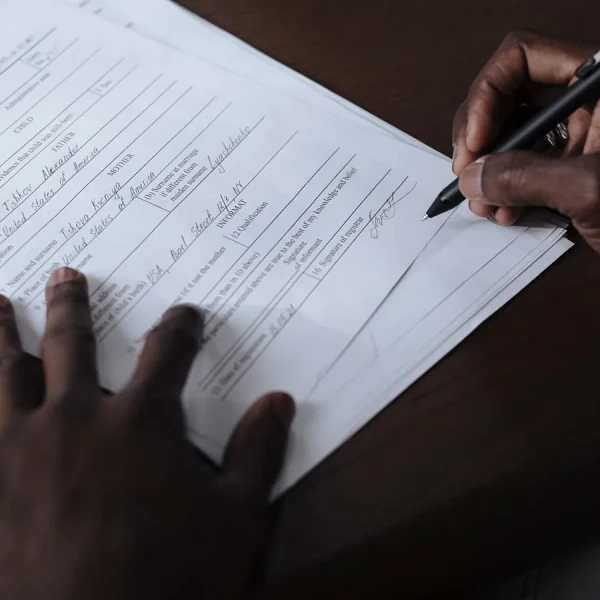 Close-up of a person signing a printed application form at a wooden desk