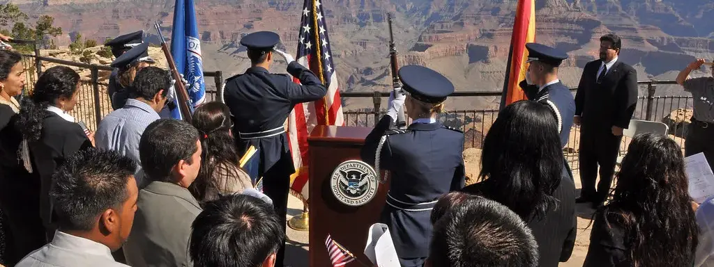 Nuevos ciudadanos durante una ceremonia de naturalización al aire libre, con la bandera de Estados Unidos al frente